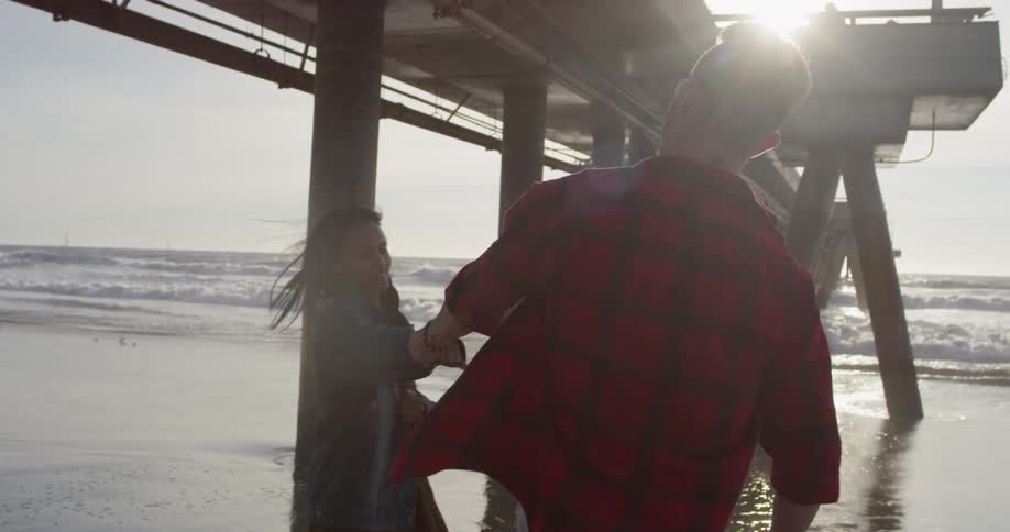 Man and woman are walking on ocean beach under pier