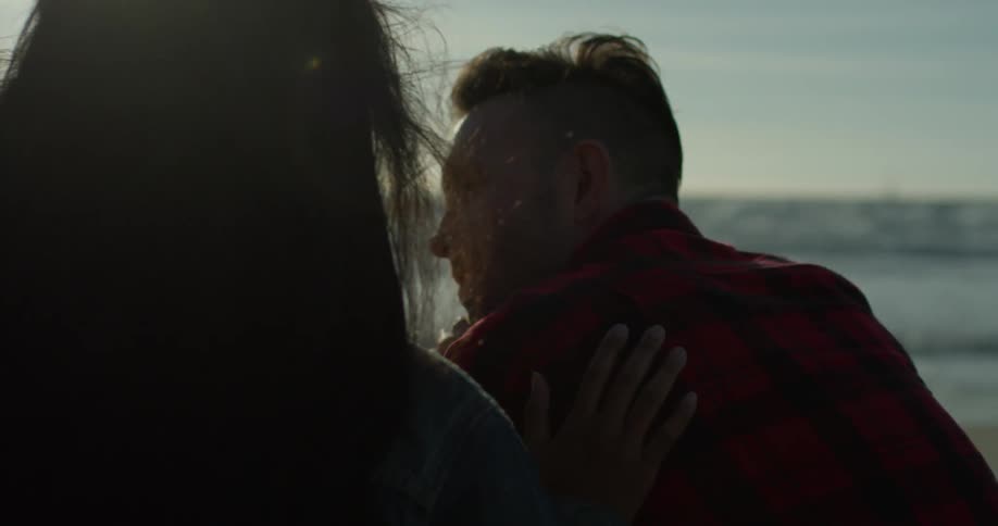 Woman is rubbing mans back while sitting on beach
