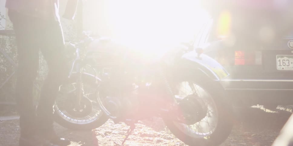 A man stands next to a motorcycle on a bright sunny day