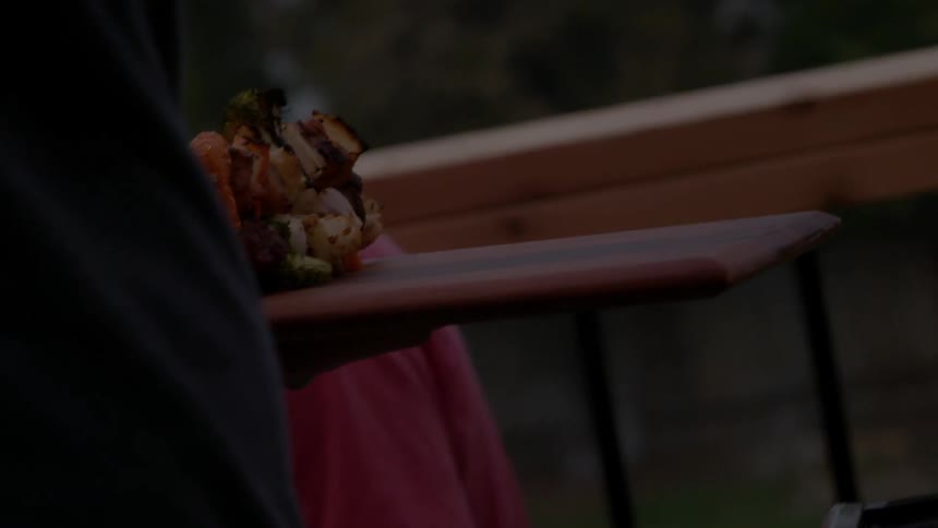 Someone using tongs to remove shish kabobs from a grill