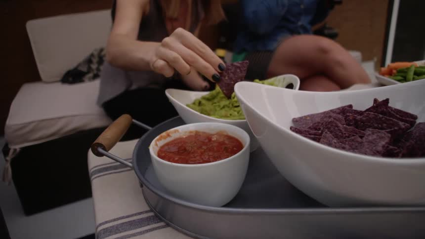 A woman reaches for a tortilla chip and then dips it into guacamole