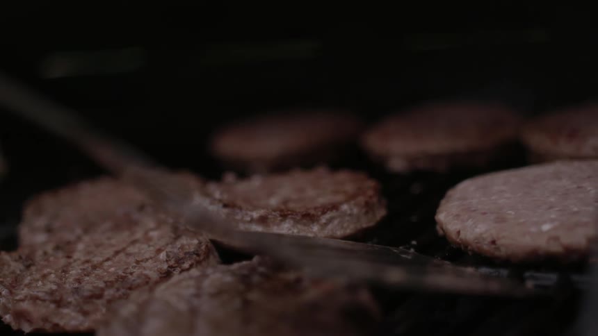 A spatula flips a burger on the grill