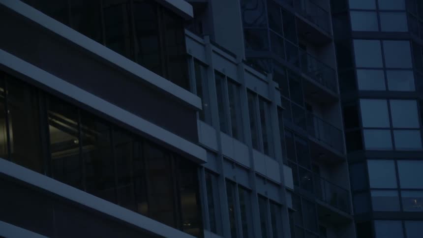 The camera pans across the front of an office building in the evening with some lights visible from inside some of the rooms