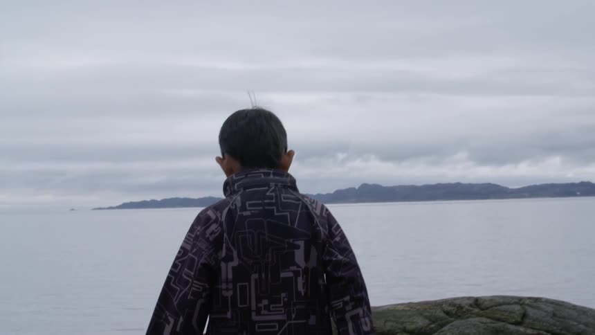 A boy walks along the rocky shore line