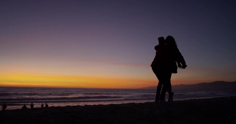 Man and woman are embracing on beach at sunset