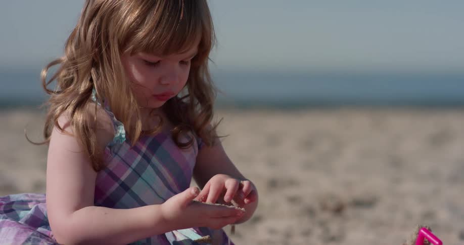 A young girl plays with sand on a beach