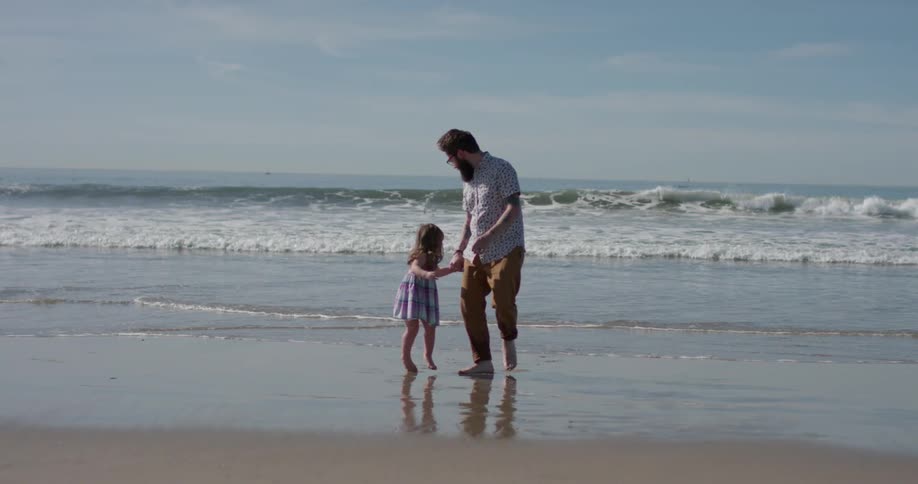 A man and young girl run on the beach
