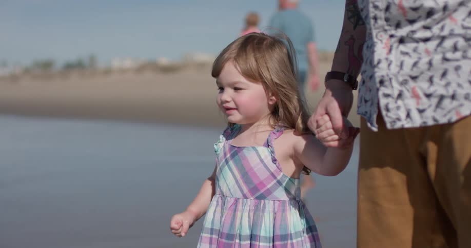 A man holds the hand of a young girl on the beach