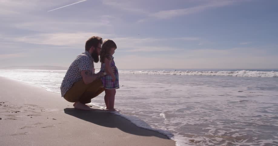 A man holds a young girl as the tide rolls in