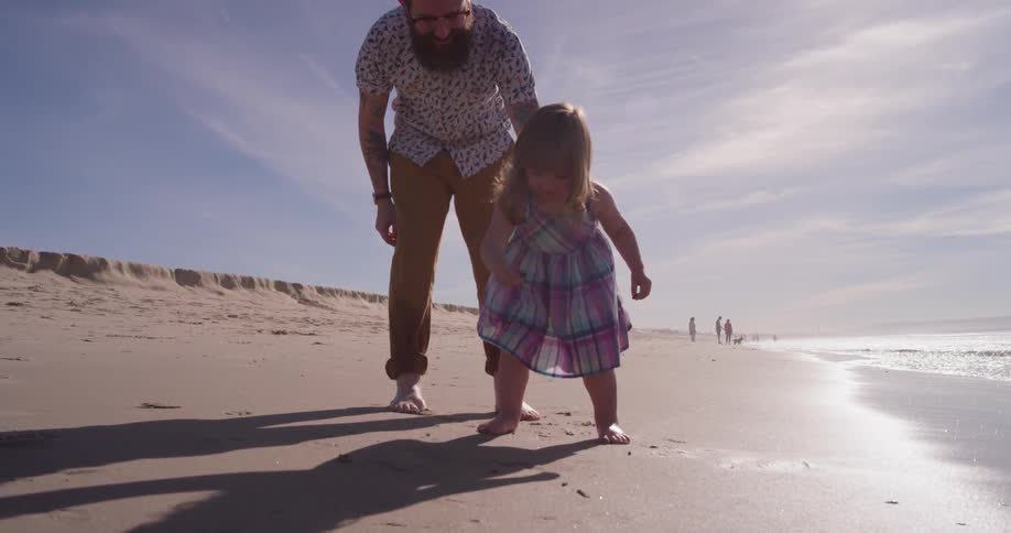 A man and young girl play on the beach