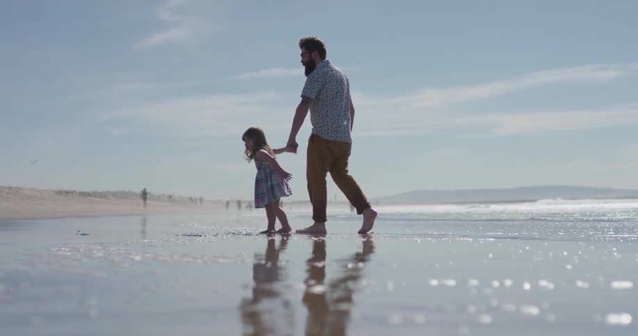 Man holds child's hand as they stand on the beach