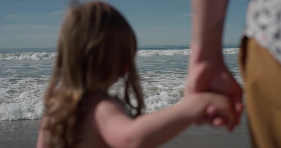 A man holds the hand of a young girl as the tide rolls in