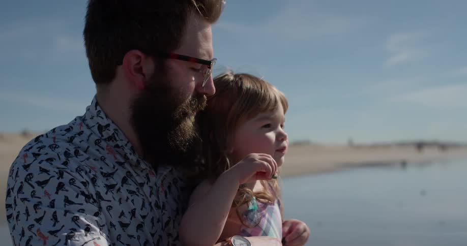 Man holds a toddler and points and talks on the beach