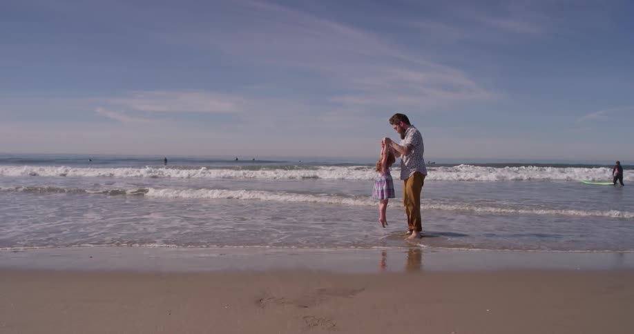 A man holds up a young girl as the tide rolls in