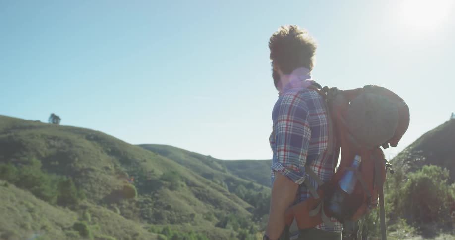 Man stands in nature on a sunny day looking out at the grassy hills