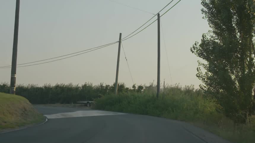 View of driving down a curved road that is surrounded by trees, brush and electric poles