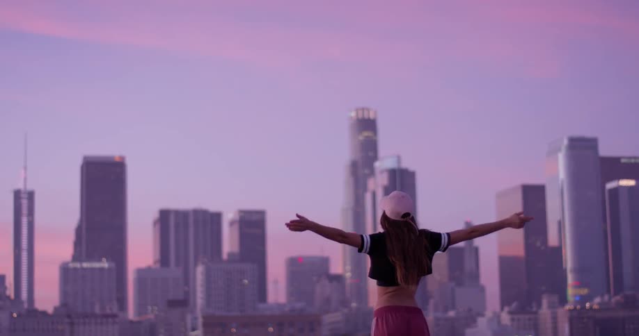 Woman jogs up to a ledge overlooking the city and stretches her arms out