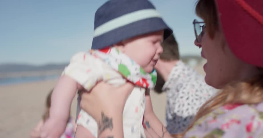 Woman holds a baby as a man and child sit nearby on the beach