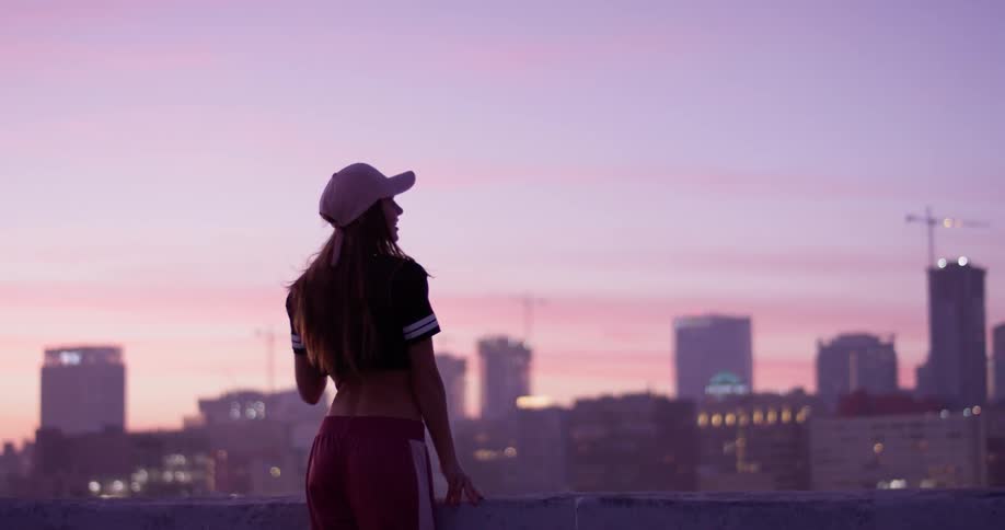 A woman is standing on a rooftop at dawn taking in an urban view