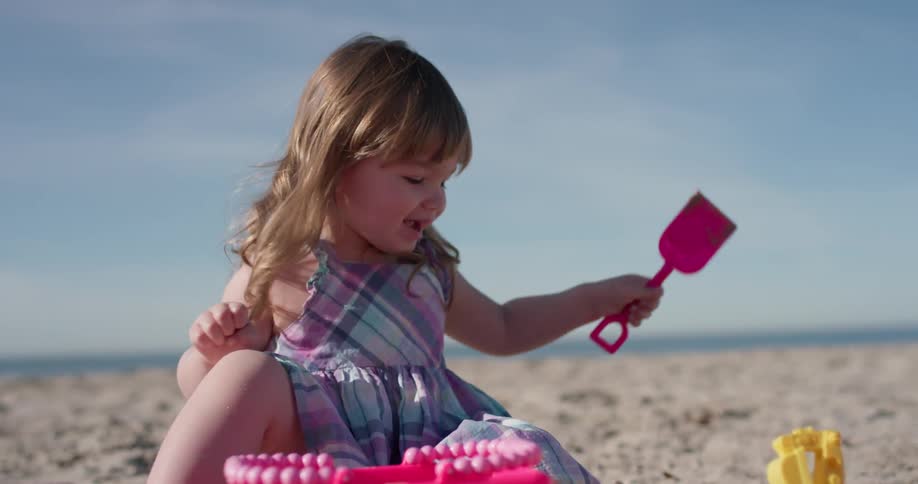 A young girl plays on the beach with plastic toys