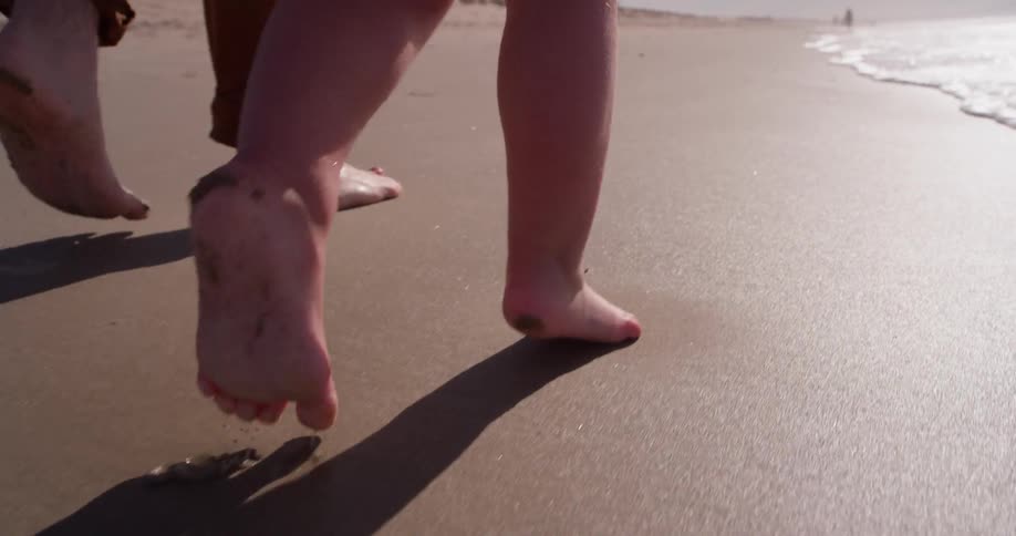 A man and young girl walk on the wet sand