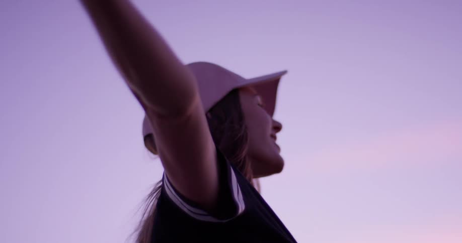 A woman in a pink hat smiles with her arms outstretched