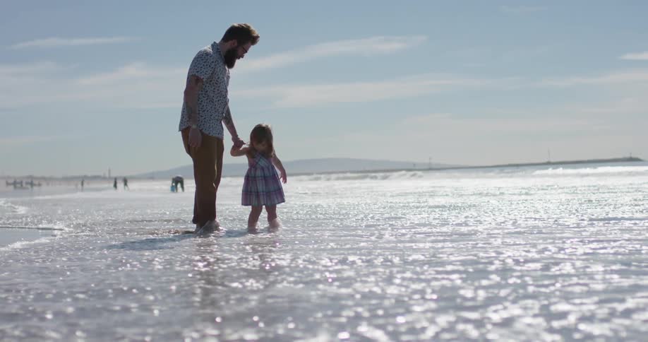 A man holds the hand of a young girl as the tide rolls in