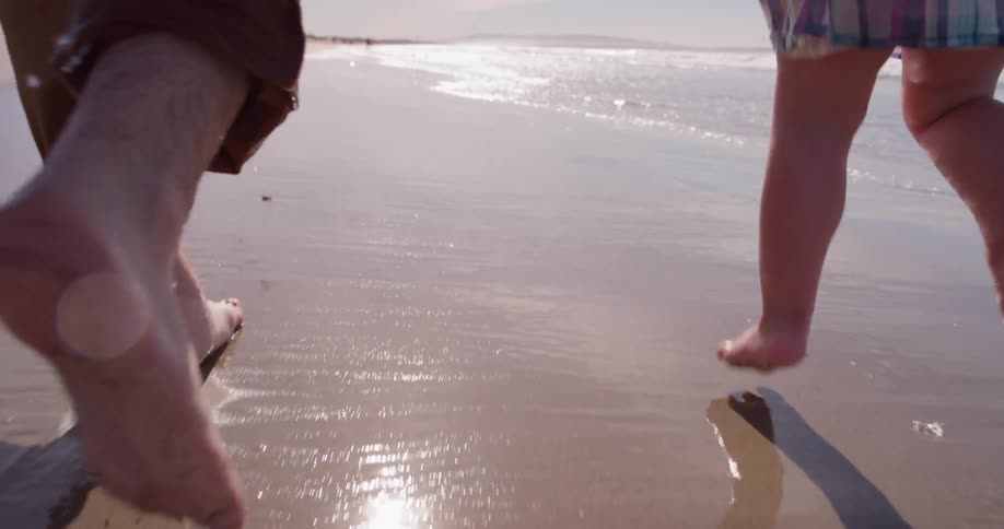 A man and young girl run on the wet sand