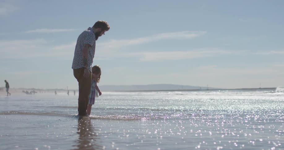 Man holds child's hand as they stand on the beach