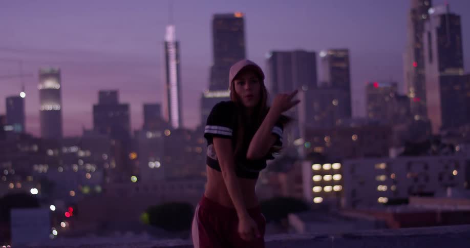 A woman is dancing on a rooftop in a city at dusk