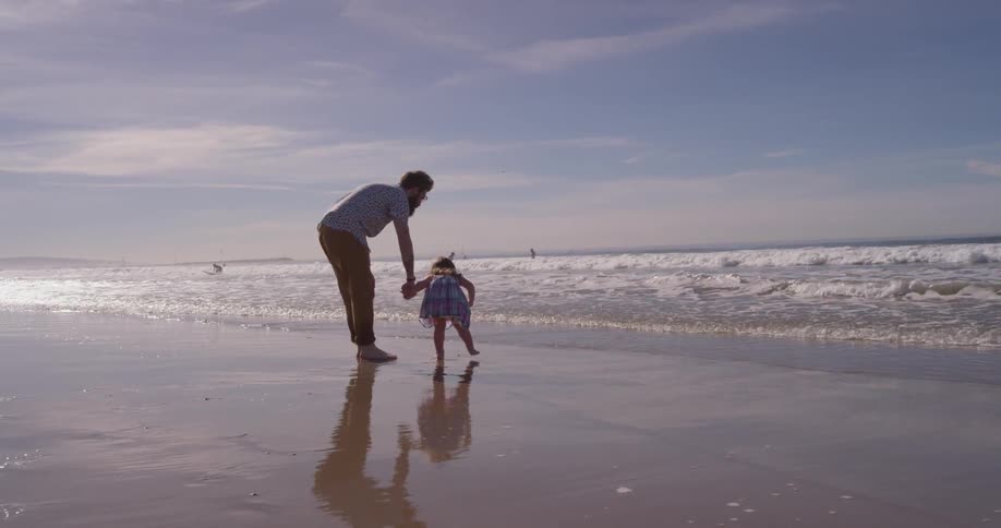 A man and young girl walk on the wet sand