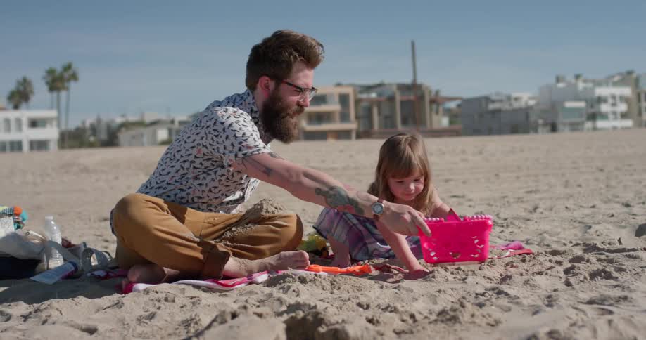 Man and toddler play in the sand on the beach