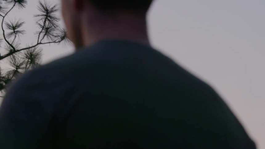 An airplane is seen flying low as the view rises from behind a man standing and staring into the distance
