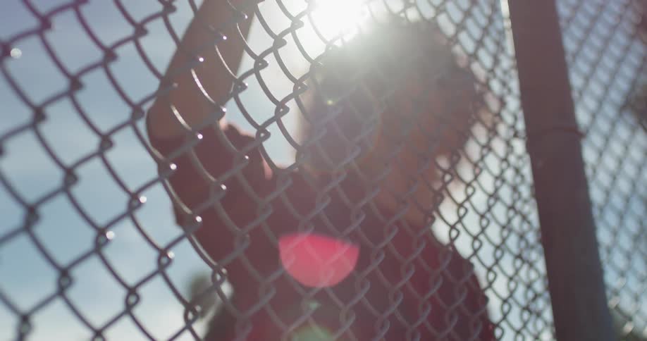 A man holds onto and looks through a chain link fence on a sunny day