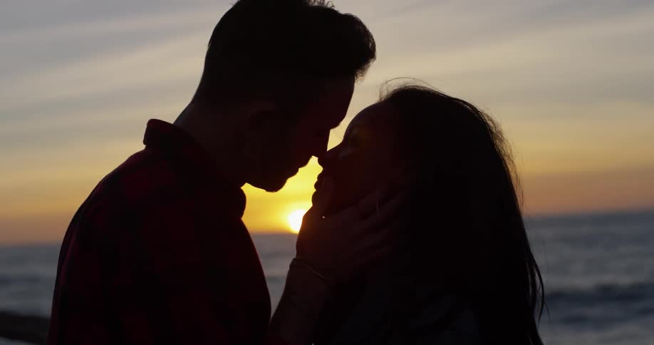 A man and woman kiss on the beach
