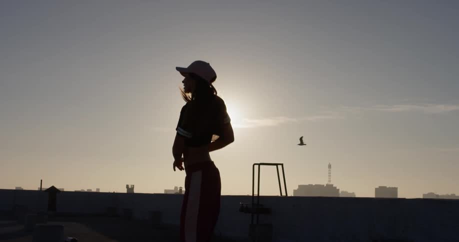 A woman in a pink hat dances on a rooftop
