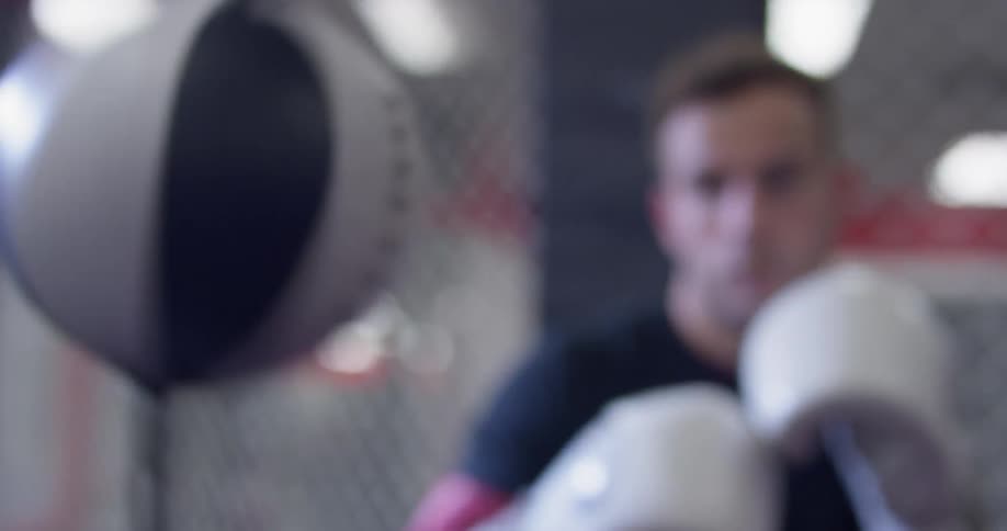 A boxer is punching a speed bag inside a gym in daylight