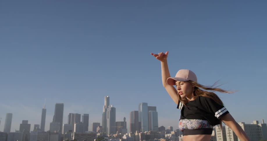 A woman in a pink hat dances on a rooftop