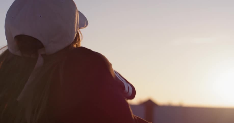 Woman stands on a rooftop at sunset waving her arms and dancing