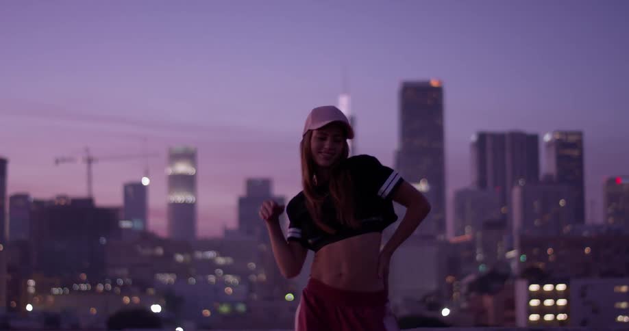 A woman is dancing on a rooftop in a city at dusk