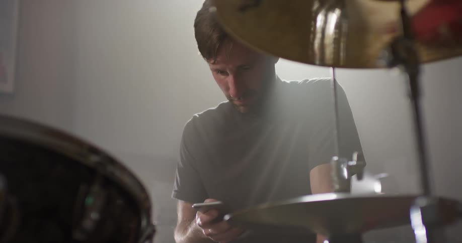 A drummer uses a phone at his drum kit
