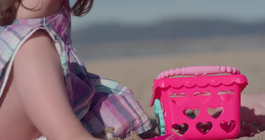 A toddler girl is playing in the sand at a beach on a sunny day