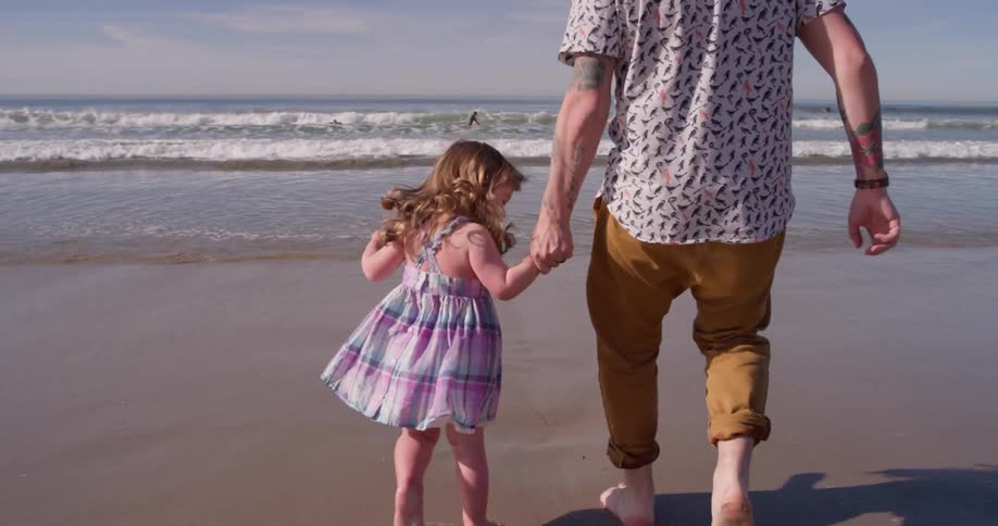 A man and young girl run playfully on the beach