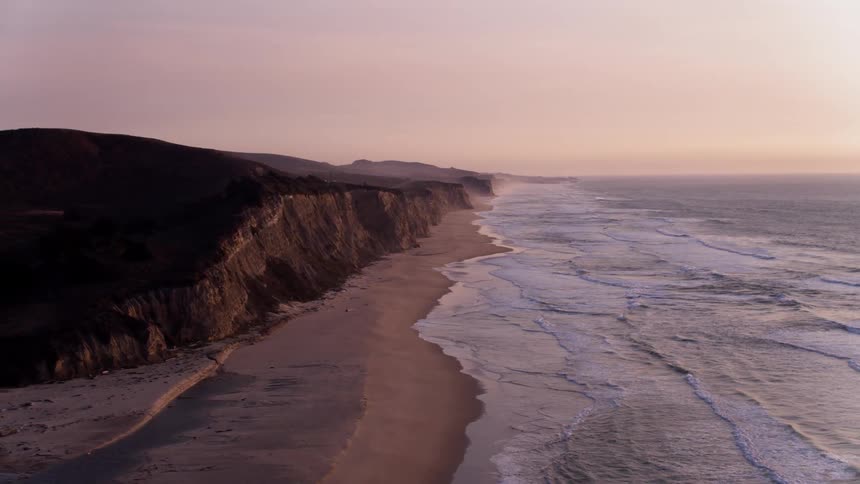 Ocean waves flow towards a shoreline at sunset