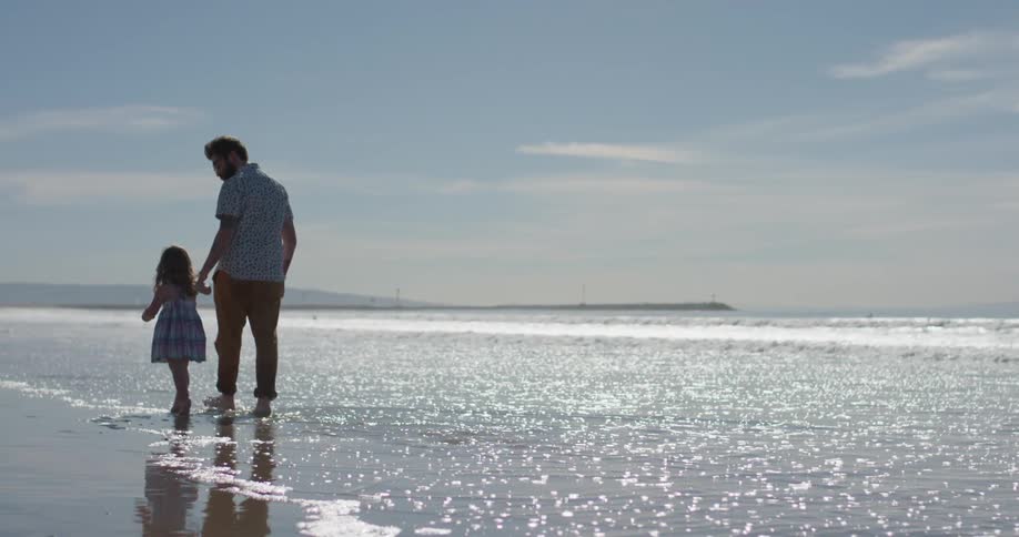 Man and toddler walk on the beach in the water on a sunny day