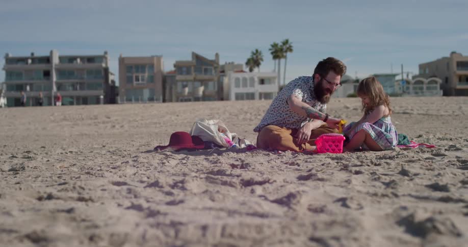 A man and young girl play with toys on the beach
