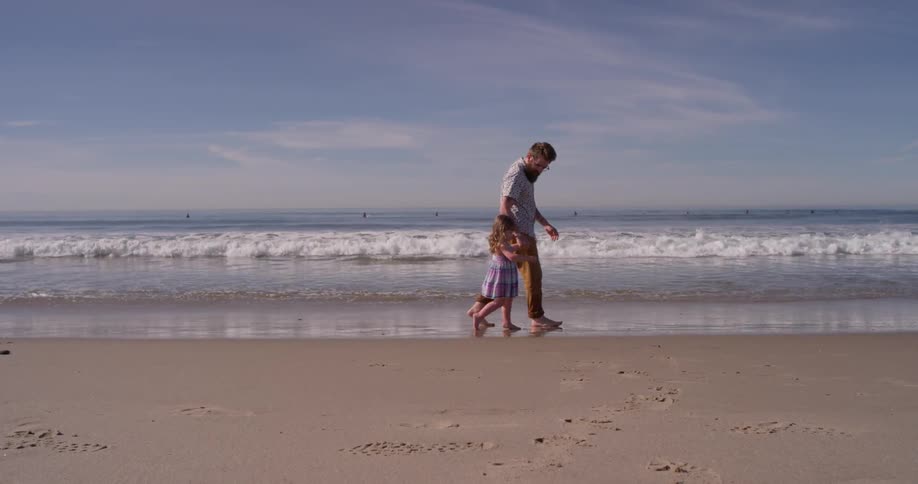A man and young girl walk on the beach