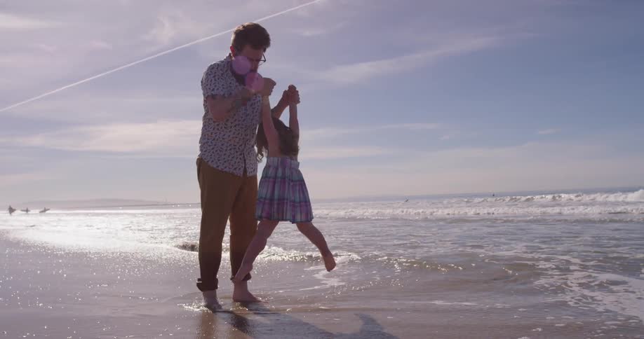 A man and young girl play on the beach