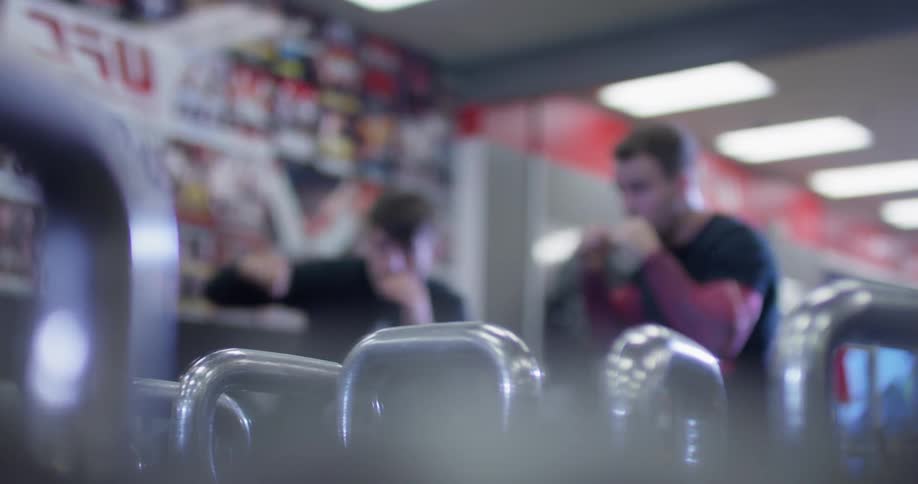 Two men are shadowboxing inside a gym in front of a mirror