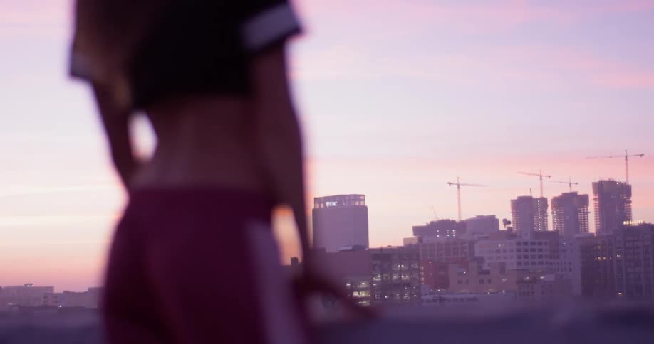 A woman is standing on a rooftop at dawn taking in an urban view